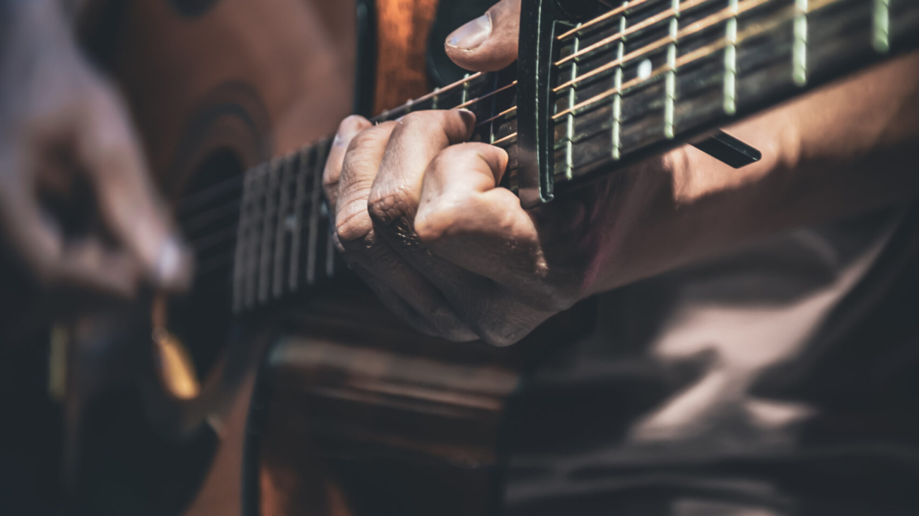 A man plays an acoustic guitar in the dark, close-up.