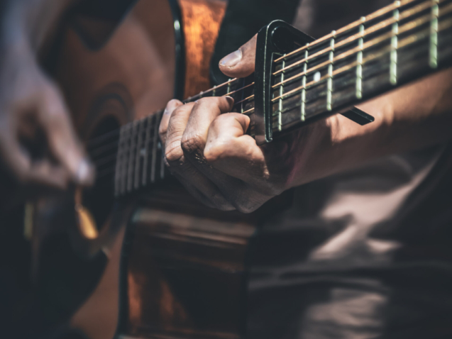 A man plays an acoustic guitar in the dark, close-up.