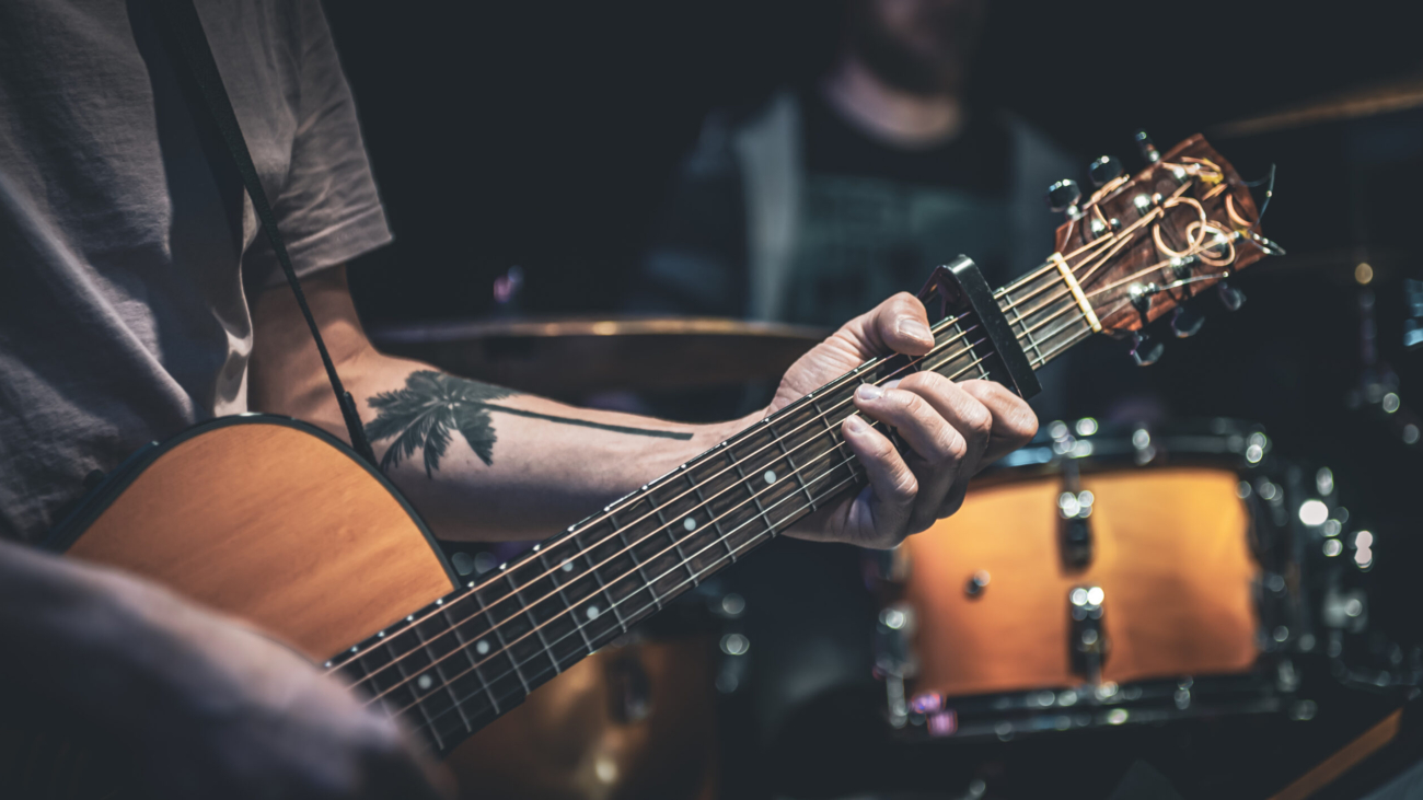 A man plays an acoustic guitar in the dark n the blurred background.