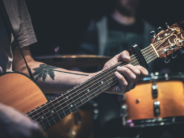 A man plays an acoustic guitar in the dark n the blurred background.